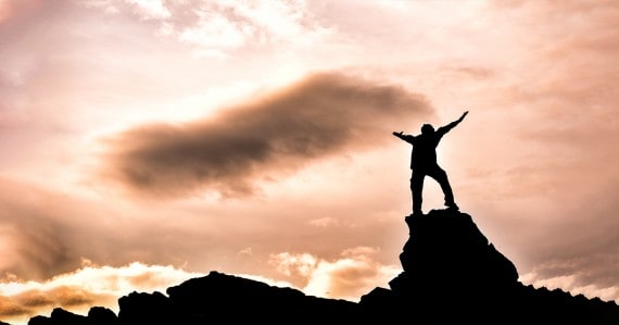 silhouetted man raising hands in victory at sunset on a rocky outcrop